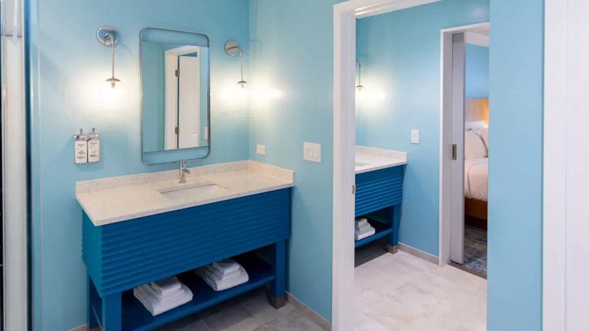 A bright, inviting bathroom with a modern blue vanity, large mirror, stylish light fixtures, and crisp white towels. The space feels clean and cheerful, ideal for refreshing showers or evening routines.