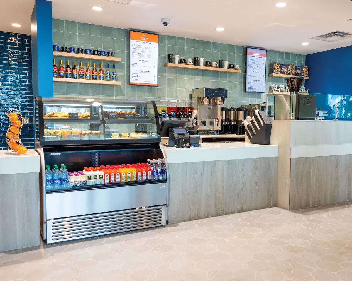 A cozy interior market space with a display case of pastries, a beverage fridge, coffee station, and menu boards. Guests enjoy freshly brewed coffee and pastries in a casual, welcoming setting.