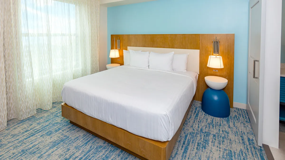 A spacious bedroom with a plush bed, elegant nightstands, thick curtains framing a window that lets in soft natural light, and a textured rug underfoot. The overall look is calm and inviting, ideal for restful nights. The design and details suggest luxury linens and ample storage.